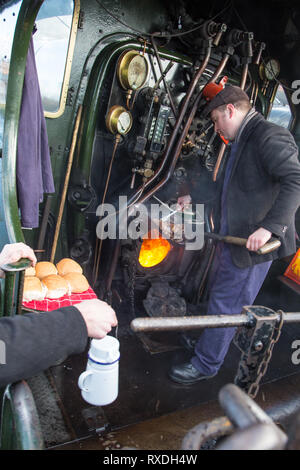 Kidderminster, Regno Unito. 9 Marzo, 2019. Nonostante la soleggiata incantesimi, si tratta di un freddo e ventilato in marzo mattina nelle Midlands. Una sorta-hearted Steam Railway macchinista sorge sulla pedana per la cottura fino hot salsicce e pancetta baps per il suo equipaggio in questa annata del motore del focolare. Come l'equipaggio capi per il giorno, in piedi la locomotiva aperto cabina, la loro colazione calda baps aiuterà certamente tenere fuori il freddo vento che sarà rivolta verso l. Credito: Lee Hudson/Alamy Live News Foto Stock