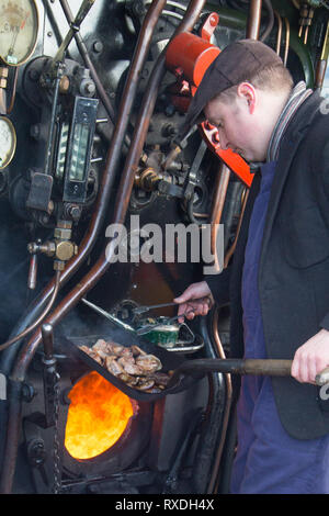 Kidderminster, Regno Unito. 9 Marzo, 2019. Nonostante la soleggiata incantesimi, si tratta di un freddo e ventilato in marzo mattina nelle Midlands. Una sorta-hearted Steam Railway macchinista sorge sulla pedana per la cottura fino hot salsicce e pancetta baps per il suo equipaggio in questa annata del motore del focolare. Come l'equipaggio capi per il giorno, in piedi la locomotiva aperto cabina, la loro colazione calda baps aiuterà certamente tenere fuori il freddo vento che sarà rivolta verso l. Credito: Lee Hudson/Alamy Live News Foto Stock