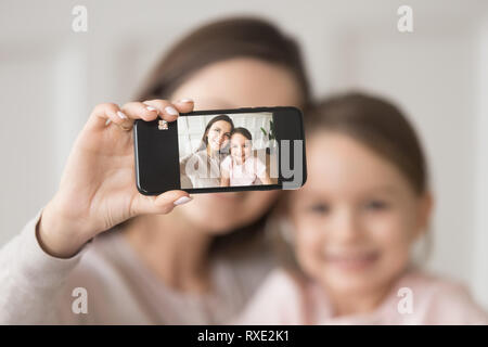 Felice madre tenendo il telefono tenendo selfie sul cellulare con la figlia Foto Stock