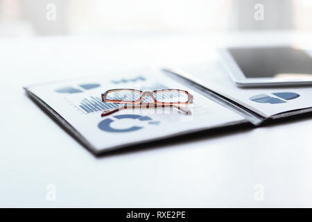 Appunti con la relazione finanziaria e i bicchieri sul desktop Foto Stock