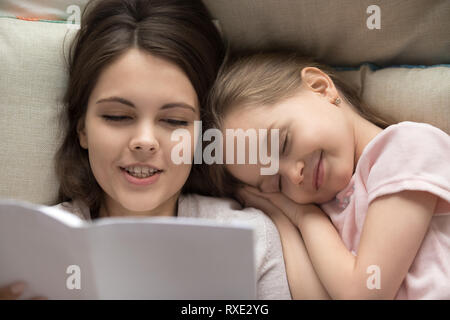 Felice bambina addormentata nel letto mamma libro di lettura Foto Stock