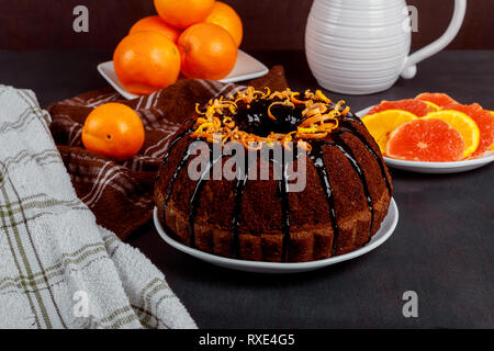 Torta al cioccolato bundt cake con glassa al cioccolato e arancia sul tagliere di legno. Primo piano Foto Stock