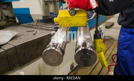 Due brillanti tubi metallici su un attrezzo magnetico. Il lavoratore mantiene l'attrezzo magnetico che trasportano i tubi e il trasporto di un'altra macchina Foto Stock