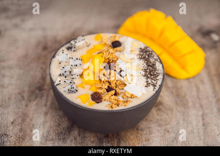 Bocce Smoothie fatta con mango, banana, granola, cocco grattugiato, dragon frutta, semi di Chia e menta su sfondo di legno. Concetto di frutta, vitamine. Foto Stock