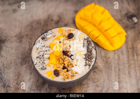 Bocce Smoothie fatta con mango, banana, granola, cocco grattugiato, dragon frutta, semi di Chia e menta su sfondo di legno. Concetto di frutta, vitamine. Foto Stock