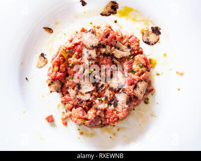 Vista superiore della carne bovina la tartare di manzo con uovo crudo e tartufo su piastra bianca in Lombardia Foto Stock