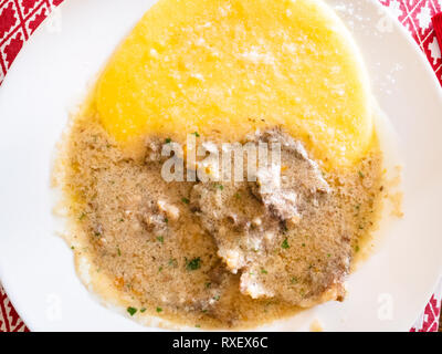 Cucina Italiana - vista superiore di manzo all'olio (stufato di manzo in salsa di olio) con polenta close up sulla piastra bianca in un ristorante locale in Lombardia Foto Stock