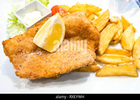 Cucina Italiana - Pollo alla Milanese (pan-fritto di pollo impanato schnitzel Milanese) con patate arrosto e limone vicino fino sulla piastra bianca in locale Foto Stock