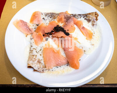 Crepes con formaggio morbido e fette di salmone decorate con artificiali di caviale nero su bianco piatto in un ristorante locale in Lombardia Foto Stock