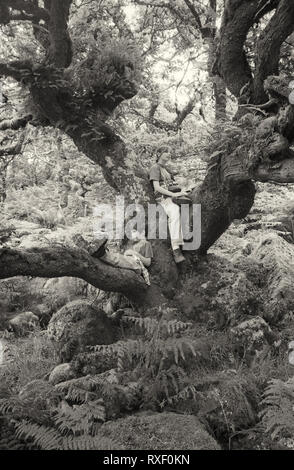 Due bambini in posa i rami di un albero in Wistman il legno sul Dartmoor Devon, Regno Unito. Film in bianco e nero della fotografia circa 1994. Modello rilasciato Foto Stock