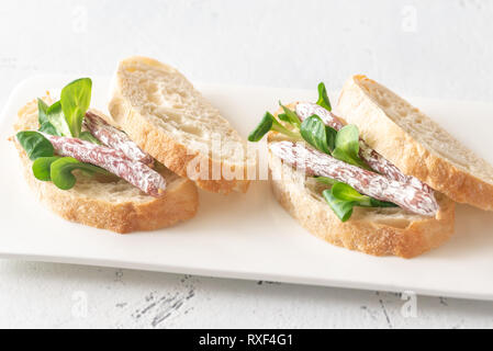 Sandwich con mini fuets e insalata di mais su sfondo bianco Foto Stock