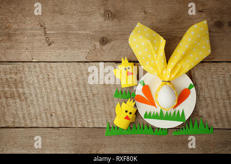 Decorazioni di pasqua i bambini tabella. Coniglietto di pasqua tenendo un tovagliolo sulla piastra su vintage sfondo di legno. Per i bambini il Progetto Arte, ricamo, artigianato per Foto Stock