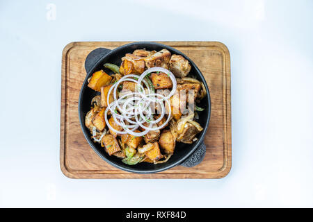 Patate fritte con carne, broccoli e cipolle rosse decorate con rosmarino in una padella su di un tavolo di legno vista dall'alto. Foto Stock