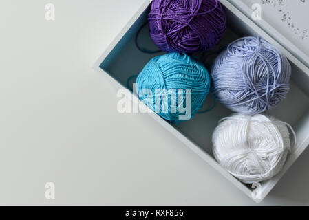 Vista da sopra il viola, blu e bianco filato per maglieria di lane in una scatola di legno con una copia spazio su uno sfondo bianco. Foto Stock