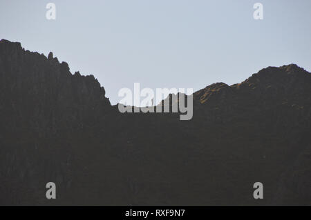 Silhouette di un escursionista solitario in piedi sul bordo di estensione sul percorso verso la Wainwright Helvellyn nel Parco Nazionale del Distretto dei Laghi, Cumbria, Inghilterra, Regno Unito. Foto Stock