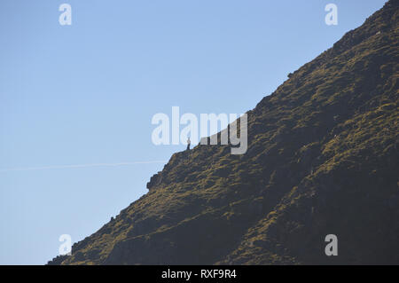 Silhouette di un escursionista solitario in piedi sul bordo di estensione sul percorso verso la Wainwright Helvellyn nel Parco Nazionale del Distretto dei Laghi, Cumbria, Inghilterra, Regno Unito. Foto Stock