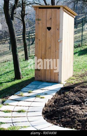 Nuovi servizi igienici in legno in giardino con il cuore del foro sagomato sulla porta. Foto Stock