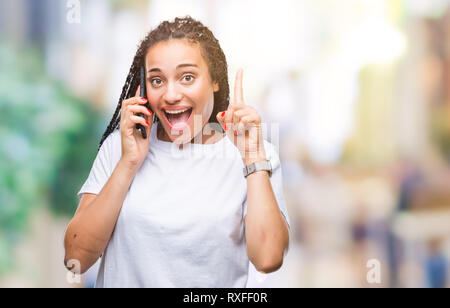 Giovani capelli intrecciati African American Girl mostra chiamando utilizza lo smartphone su sfondo isolato sorpreso con un'idea o domanda puntare il dito Foto Stock