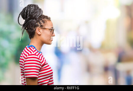 Giovani capelli intrecciati African American Girl indossando occhiali su sfondo isolato guardando al lato, profilo relax posano con faccia naturale con fiduciosa Foto Stock