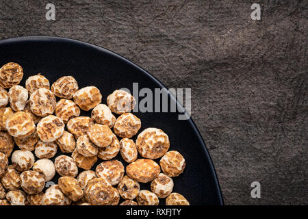 Sbucciate organico tiger dadi, una ricca fonte di amido resistente, vista dall'alto su una piastra nera contro la trama della carta di corteccia Foto Stock