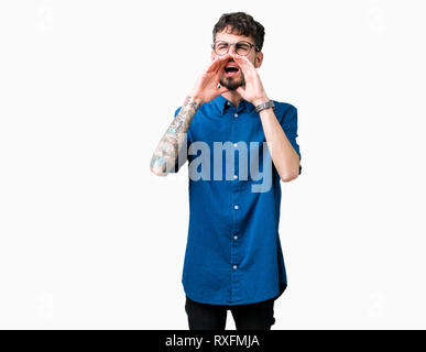 Giovane uomo bello con gli occhiali più isolato che urlava arrabbiato ad alto volume con Mani sulla bocca Foto Stock