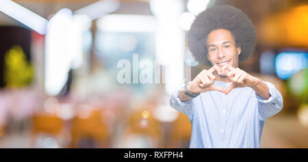 Giovane americano africano uomo con capelli afro sorridente in amore che mostra il simbolo del cuore e la forma con le mani. Concetto romantico. Foto Stock