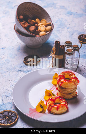 Foto verticale con varie ciambelle preparate dalla pasta sfoglia di pasta alimentare. Rosso fragola topping è versato sul ring. Le ciambelle sono poste su piastra bianca con pochi Foto Stock