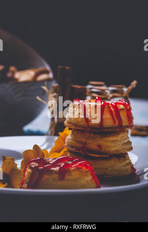 Foto verticale con varie ciambelle preparate dalla pasta sfoglia di pasta alimentare. Rosso fragola topping è versato sul ring. Le ciambelle sono poste su piastra bianca con pochi Foto Stock