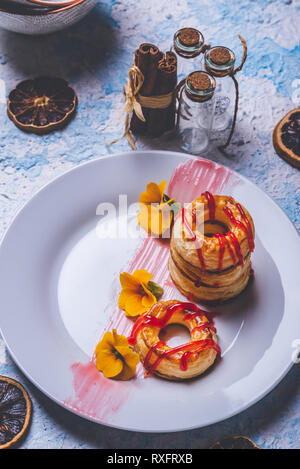 Foto verticale con varie ciambelle preparate dalla pasta sfoglia di pasta alimentare. Rosso fragola topping è versato sul ring. Le ciambelle sono poste su piastra bianca con pochi Foto Stock