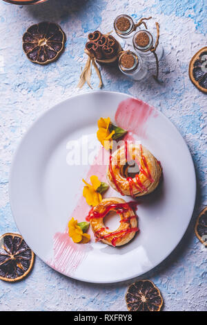 Foto verticale con vista dall'alto su diversi ciambelle preparate dalla pasta sfoglia di pasta alimentare. Rosso fragola topping è versato sul ring. Le ciambelle sono collocati su bianco pla Foto Stock