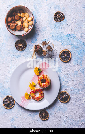 Foto verticale con vista dall'alto su diversi ciambelle preparate dalla pasta sfoglia di pasta alimentare. Rosso fragola topping è versato sul ring. Le ciambelle sono collocati su bianco pla Foto Stock