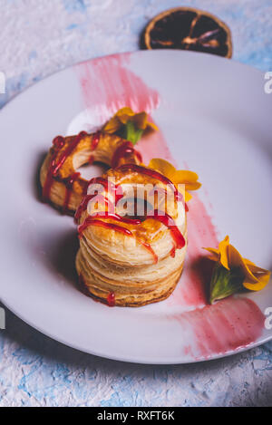 Foto verticale con varie ciambelle preparate dalla pasta sfoglia di pasta alimentare. Rosso fragola topping è versato sul ring. Le ciambelle sono poste su piastra bianca con pochi Foto Stock