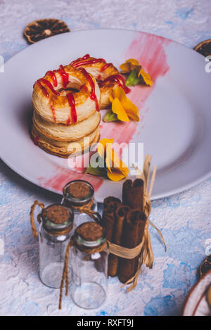 Foto verticale con varie ciambelle preparate dalla pasta sfoglia di pasta alimentare. Rosso fragola topping è versato sul ring. Le ciambelle sono poste su piastra bianca con pochi Foto Stock