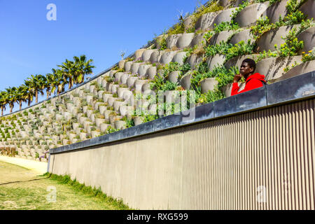 Valencia Central Park quartiere Russafa un uomo afro-americano in abiti rossi guarda allo spazio, Spagna Europa Foto Stock