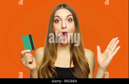 Sorpreso eccitato stupiti donna giovane azienda carta di credito su sfondo arancione Foto Stock