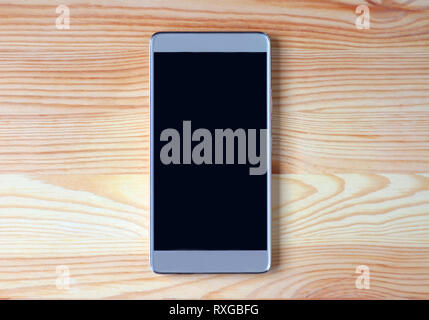 Vista dall'alto di un nero vuota nella schermata smartphone isolato sul marrone chiaro Tavolo in legno Foto Stock