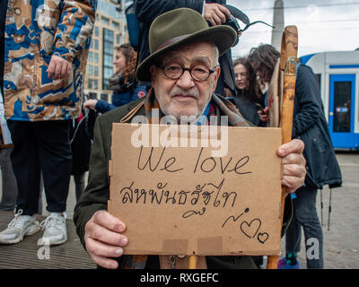 Un vecchio uomo è visto seduto mentre tenendo un cartello che dice che amiamo durante la protesta. Un giorno dopo la giornata internazionale della donna una dimostrazione sotto il motto "tutte le oppressioni è collegato', ha avuto luogo presso il centro di Amsterdam. Centinaia di persone si sono radunate a Dam Square a fare una dichiarazione per il loro diritto di essere chi sono, tra cui vivere senza paura e con rispetto, la parità di retribuzione e avente lo stesso diritto alla giustizia a prescindere dal colore della pelle, di reddito, di religione o di capacità. Foto Stock