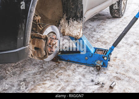 Il processo di lavoro di rimozione delle ruote dalla macchina sulla strada in inverno. Sostituzione di pneumatici invernali per l'estate con un martinetto. Foto Stock