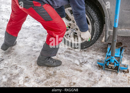 Il processo di lavoro di rimozione delle ruote dalla macchina sulla strada in inverno. Sostituzione di pneumatici invernali per l'estate con un martinetto. Foto Stock