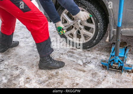 Il processo di lavoro di rimozione delle ruote dalla macchina sulla strada in inverno. Sostituzione di pneumatici invernali per l'estate con un martinetto. Foto Stock