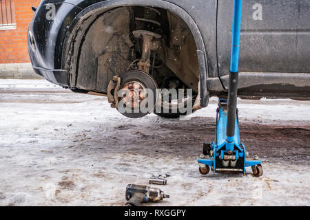 Il processo di lavoro di rimozione delle ruote dalla macchina sulla strada in inverno. Sostituzione di pneumatici invernali per l'estate con un martinetto. Foto Stock