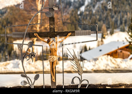 LA VILLA (BZ), Italia - 9 febbraio 2019: la luce solare è illuminante la statua di Gesù crocifisso sulla tomba nel cimitero Foto Stock