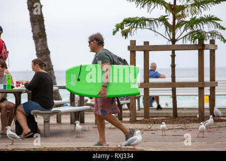 Medio di sesso maschile di età compresa tra i surfer a piedi attraverso Manly Beach a Sydney, Australia Foto Stock