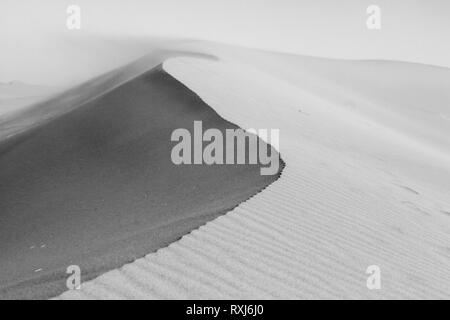 Dune ridge dettaglio, vicino. Increspature di sabbia e texture. La sabbia nel vento sullo sfondo. Deserto del Sahara. Il Marocco. Bianco e nero, monocromatiche. Foto Stock