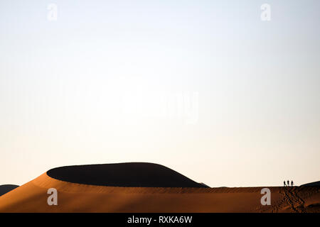 Tre persone si stagliano sulla sommità di una duna in Sossusvlei. Foto Stock