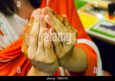 Una donna caucasica coppettazione le mani per mostrare il mehndi disegni su di lei le dita indice. Bokeh di fondo per la creatività. Shilparamam, Hyderabad, Telangana, India. Foto Stock