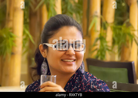 Un close up ritratto di una bella e giovane, fiducioso, professional donna indiana con il designer di occhiali, acqua potabile in un ristorante a pranzo. Foto Stock