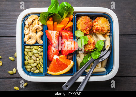 Cibo sano e scatola di pranzo. Pasto sano prep contenitori con polpette di fagioli, pasta, verdure, frutti di bosco, semi e noci in un contenitore su un backgro scuro Foto Stock