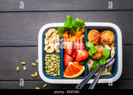 Cibo sano e scatola di pranzo. Pasto sano prep contenitori con polpette di fagioli, pasta, verdure, frutti di bosco, semi e noci in un contenitore su un backgro scuro Foto Stock