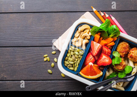 Scatola di pranzo per la scuola. Pasto sano prep contenitori con polpette di fagioli, pasta, verdure, frutti di bosco, semi e noci in un contenitore su un backgroun scuro Foto Stock